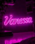 Scritta luminosa neon rosa con il nome Vanessa appesa alla parete sopra una scrivania